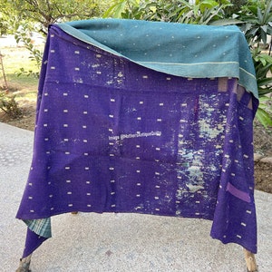 May include: A purple kantha quilt with white dots and a green border. The quilt is folded in half and draped over a wooden frame. The quilt is made of recycled saris and is a traditional Indian textile.