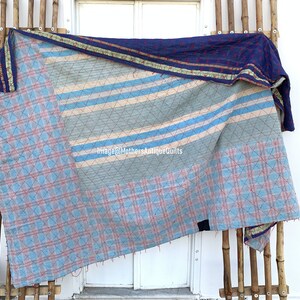 May include: A blue and white kantha quilt with a striped pattern and a checkered pattern. The quilt is hanging on a bamboo rack.