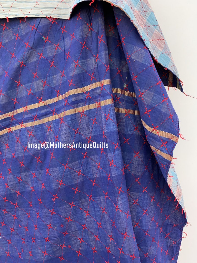 May include: A blue kantha quilt with red embroidered stars and two gold stripes. The quilt is folded and shows the back side, which is a plaid pattern.