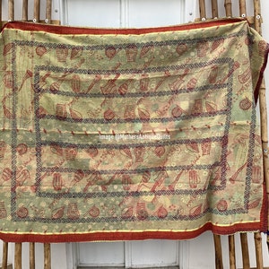 May include: A vintage quilt with a repeating pattern of musical instruments and other objects in red and green on a cream background. The quilt has a red border and is displayed on a bamboo frame.