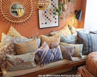 May include: A wooden bench with a variety of colorful patterned pillows. The bench is in a room with a light brown wall and a white rug. The text "IMAGE @MOTHERS ANTIQUE QUILTS" is visible on the bench.