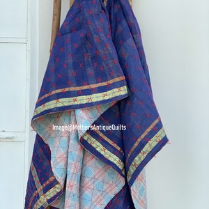 May include: A blue and white kantha quilt with red stitching and gold trim. The quilt is folded and draped over a wooden rack. Image@MothersAntiqueQuilts