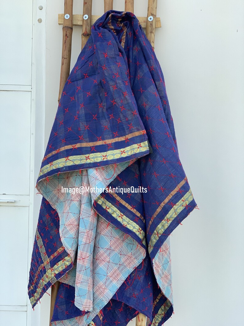 May include: A blue and white kantha quilt with red stitching and gold trim. The quilt is folded and draped over a wooden rack. Image@MothersAntiqueQuilts