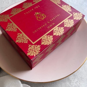 Puede incluir: Caja de regalo de boda roja y dorada con un dise&ntilde;o dorado y el texto "Thank You" "Shivayann & Babitha" y "10.02.24".