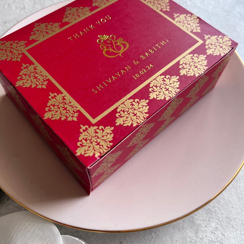 Puede incluir: Caja de regalo de boda roja y dorada con un dise&ntilde;o dorado y el texto "Thank You" "Shivayann & Babitha" y "10.02.24".
