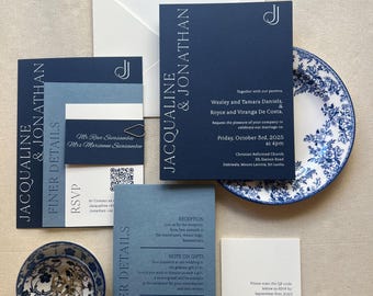 May include: Navy blue wedding invitation suite with the names Jacqueline & Jonathan. Includes RSVP cards, reception details, and a decorative plate with a blue floral design. The suite also includes a small bowl with gold rings.