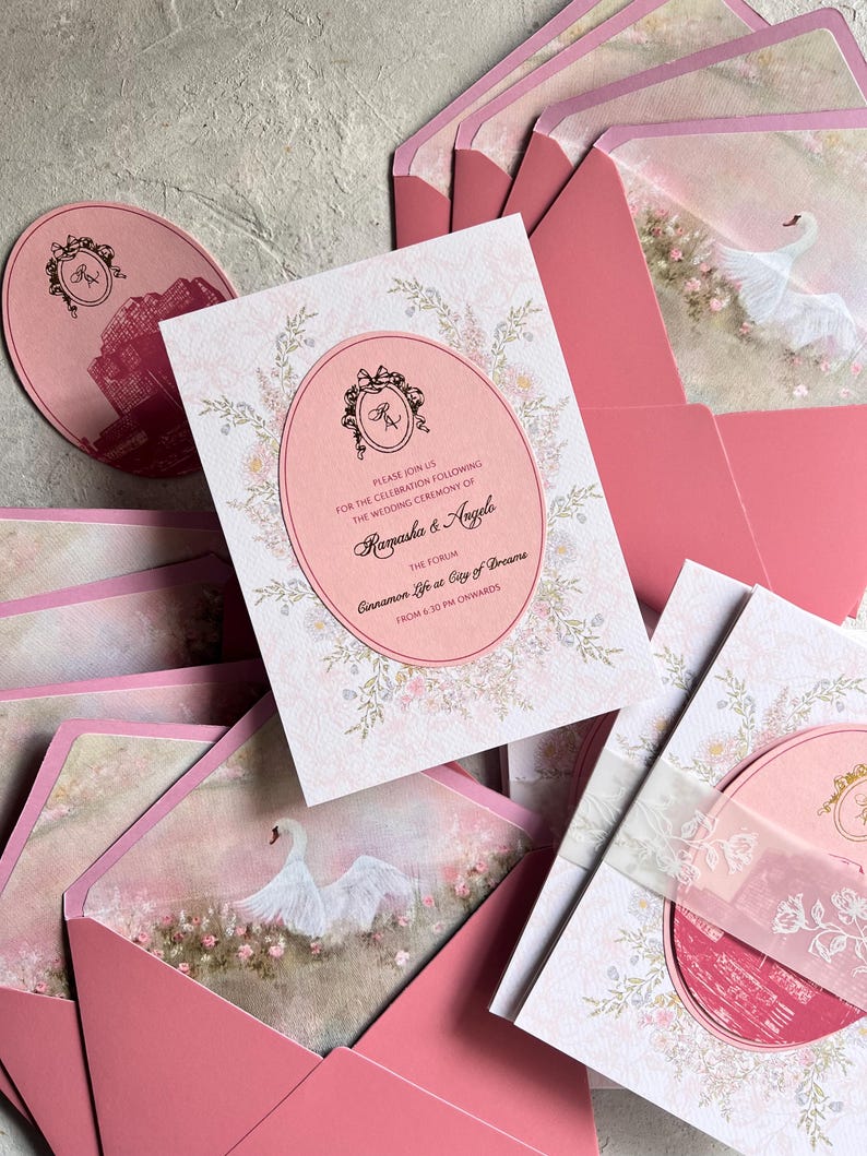 May include: Pink wedding invitations and envelopes. The invitation features an oval design with floral accents and the text "Ramasha & Angelo". The envelopes have a swan illustration. A matching round card is also visible.