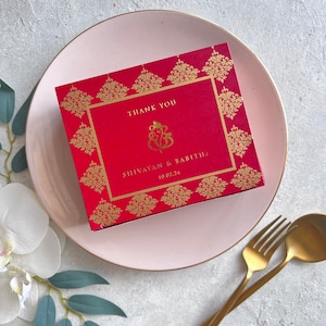 May include: A red thank you card with gold accents and a traditional Indian design. The card says "Thank You" and features the names "Shivayan & Babitha" and the date "10.02.24".