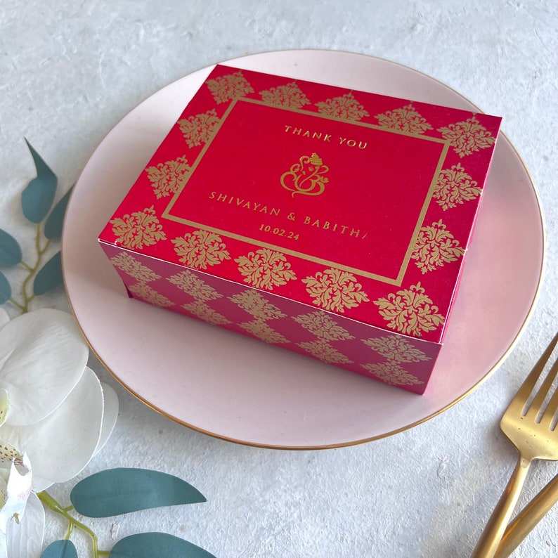 Puede incluir: Caja de regalo de boda roja y dorada con un dise&ntilde;o de Ganesha dorado y el texto "Gracias Shivayam & Babitha 10.02.24"