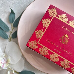 Puede incluir: Tarjeta de agradecimiento roja con detalles en dorado y un s&iacute;mbolo de Ganesha dorado. La tarjeta dice "Gracias" y "Shivayan & Sabitha" con la fecha "10.02.24".