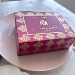 Puede incluir: Una caja de color burdeos con detalles dorados y un dise&ntilde;o dorado. La caja tiene un mensaje de agradecimiento con el texto "THANK YOU" y "SHIVAYAN & BABITHA" con la fecha "10.02.24".