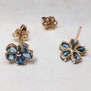 May include: A pair of gold flower-shaped earrings with blue gemstones. Each earring has a post and a butterfly-shaped back.