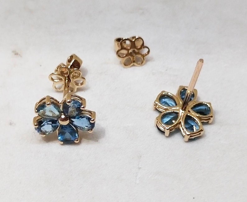 May include: A pair of gold flower-shaped earrings with blue gemstones. Each earring has a post and a butterfly-shaped back.
