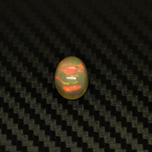 May include: A white oval opal gemstone with a red, green, and blue iridescent sheen.