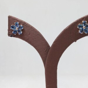 May include: A pair of blue sapphire flower stud earrings on a brown display stand.