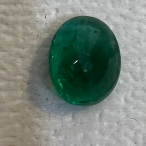 May include: A vibrant green oval-shaped gemstone with a smooth, polished surface.