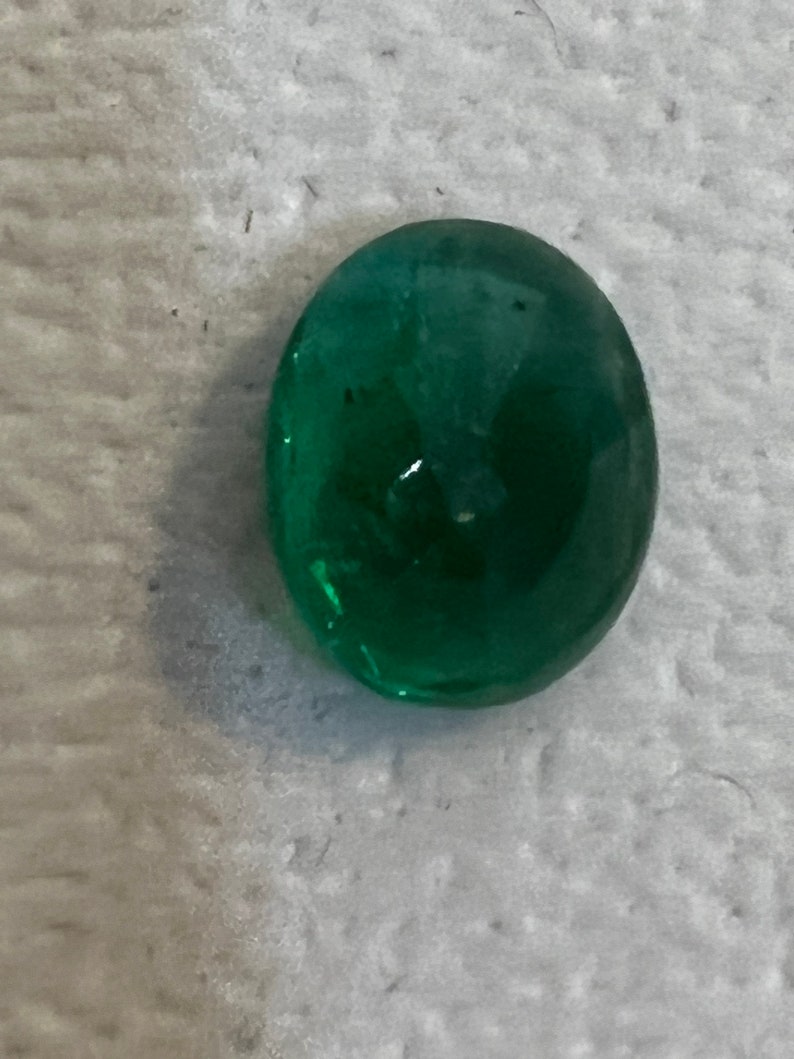 May include: A vibrant green oval-shaped gemstone with a smooth, polished surface.