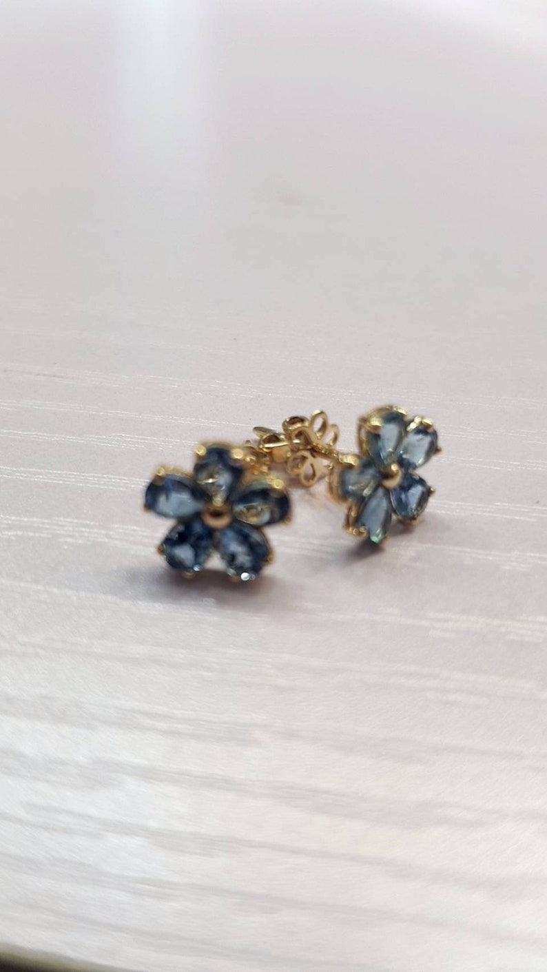 May include: A pair of gold flower-shaped earrings with blue gemstones.