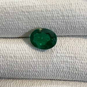 May include: A vibrant green oval-shaped emerald gemstone.