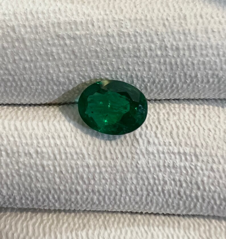 May include: A vibrant green oval-shaped emerald gemstone.
