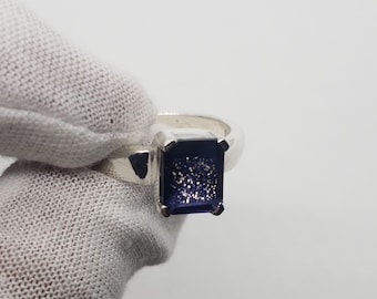 May include: A silver ring with a dark blue gemstone set in a square shape.