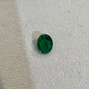 May include: A vibrant green emerald gemstone, cut into an oval shape.