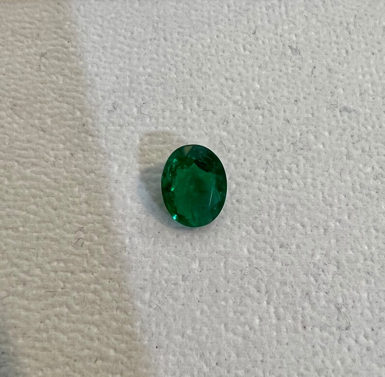 May include: A vibrant green emerald gemstone, cut into an oval shape.