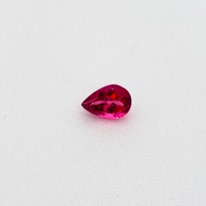 May include: A pear-shaped, pink gemstone with a faceted cut.