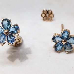 Puede incluir: Un par de pendientes de oro en forma de flor con piedras preciosas azules. Cada pendiente tiene seis piedras preciosas en forma de flor.