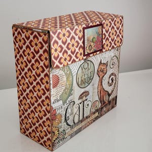 Könnte beinhalten: Eine dekorative Box mit Klappdeckel. Die Box hat ein sich wiederholendes geometrisches Muster in Braun- und Orangetönen. Die Frontplatte zeigt eine Katzenillustration und die Worte "You Are Unique" und "Cat".