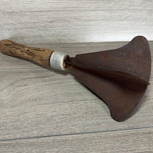 May include: A vintage, rusty metal garden tool with a wooden handle. The tool has a wide, flat blade with a rounded tip.