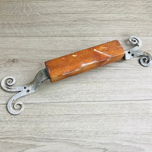 Puede incluir: Un tirador de puerta de madera con volutas de metal en cada extremo. El tirador es marrón y las volutas son plateadas.