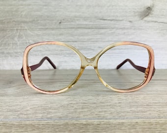 May include: A pair of large, round, clear spectacles with a burgundy rim. The glasses have a retro style.