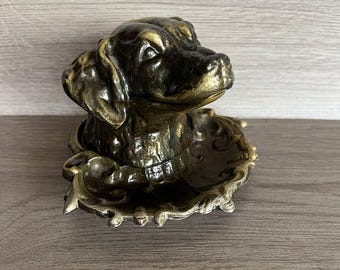 May include: A bronze dog head sculpture with a decorative base. The dog is looking to the right and has a detailed face.