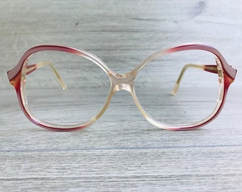 May include: A pair of clear plastic spectacles with a pink rim. The glasses have a rounded, oval shape.