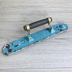 May include: A vintage door handle with a blue metal plate and a wooden handle with brass accents. The handle is slightly rusted and shows signs of wear.