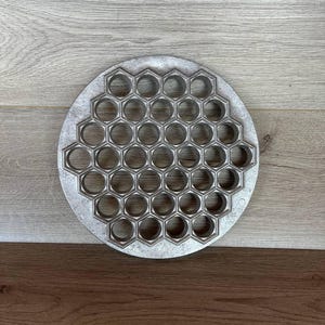 May include: A round metal mold with a honeycomb pattern of 27 circular cutouts. The mold is silver in color and has a smooth surface.