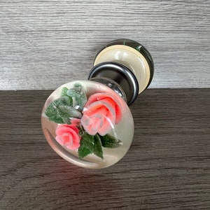 Può includere: Un pomello di vetro trasparente con un design floreale. Il pomello presenta rose rosa e foglie verdi.