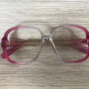 May include: Pink and clear plastic glasses with a rounded frame. The glasses have a gradient color from pink to clear.