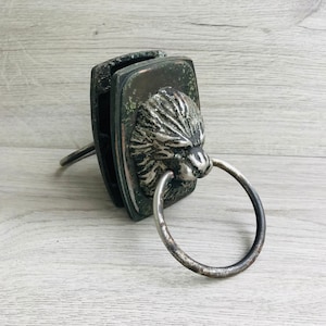 Peut inclure: Un heurtoir de porte en argent avec un motif de tête de lion. Le heurtoir est fixé à une porte en bois.