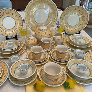 May include: A set of yellow and green patterned ceramic dinnerware, including plates, bowls, cups, saucers, and a teapot. The set features a decorative design with a yellow background and green accents.
