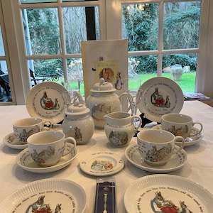 Può includere: Un set da tè in porcellana bianca con illustrazioni di Peter Rabbit. Il set comprende una teiera, un creamer, uno zuccheriera, quattro tazze da tè e piattini. Le tazze da tè e i piattini hanno un bordo ondulato e presentano un bordo con il testo "Once upon a time there were four little Rabbits, and their names were Flopsy, Mopsy, Cotton-tail and Peter."