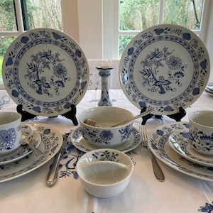 Può includere: Un set di tazze da tè, piattini e piatti in porcellana blu e bianca con un motivo floreale. Il set comprende una ciotola per la zuppa e un piccolo piatto.