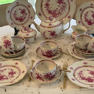 May include: A vintage tea set featuring a pink floral pattern with gold accents. The set includes a teapot, sugar bowl, creamer, cups, saucers, and plates. The plates have a decorative, scalloped edge.