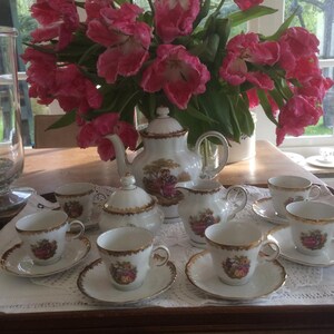 May include: A white porcelain tea set with gold trim and floral designs. The set includes a teapot, creamer, sugar bowl, and six teacups and saucers.