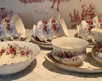 May include: A vintage tea set featuring white porcelain cups, saucers, a creamer, and a serving bowl. Each piece is adorned with a delicate pink rose pattern and gold trim, creating an elegant and classic aesthetic. The set is ideal for serving tea.