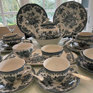 Pode incluir: Um conjunto de louça de cerâmica branca com um padrão floral azul escuro em transferência. O conjunto inclui um bule, pratos grandes, chávenas com pires a condizer, taças e um tabuleiro retangular, todos decorados com motivos botânicos detalhados.