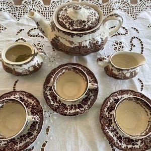 Könnte beinhalten: Ein Set aus braunen und weißen, floral gemusterten Teetassen, Untertassen, einer Teekanne und einem Milchkännchen. Die Teetassen und Untertassen haben ein braunes Blumenmuster auf weißem Hintergrund. Die Teekanne und das Milchkännchen haben ein weißes Blumenmuster auf braunem Hintergrund.