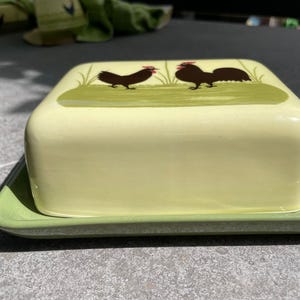Peut inclure: Un beurrier en c&eacute;ramique vert et blanc avec un motif de coq. Le beurrier a un couvercle et une base.