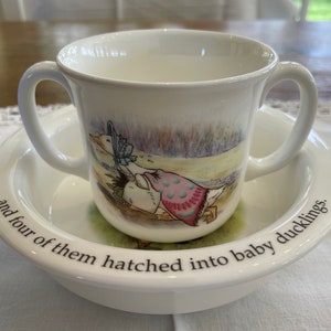 Puede incluir: Conjunto de taza y platillo de cerámica blanca para niños con una ilustración de Beatrix Potter de una madre pato y patitos. El platillo tiene el texto "and four of them hatched into baby ducklings."